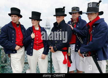 United States Coast Guard, die Seeleute in 1812 Uniformen auf einem Pier stehen, als die USS Constitution, Hintergrund Mitte im Hafen von Boston auf seiner jährlichen Unabhängigkeitstag Wende in Boston, Massachusetts, Mittwoch, 4. Juli 2012 Segel. Das diesjährige Juli 4. feiern mit den 200. Jahrestag des Krieges von 1812 zusammenfallen. Verfassung ist berühmt für ihre Handlungen während des Krieges, wenn sie zahlreiche Handelsschiffe erfasst und fünf britische Kriegsschiffen besiegt. Stockfoto