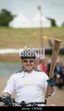 6. Juli 2012, Hadleigh Farm, Essex. Die Olympische Fackel durchläuft der Olympischen Mountainbike Veranstaltungsort Dan Jarvis die Fackel um einen Abschnitt des Rennens findet route mit dem Mountainbike vor Übergabe an Läufer Kim Axford (nicht abgebildet). und ab in Richtung Basildon und Grautöne. Das Wetter wurde zu trocken und sonnig, wie die Fackel am Veranstaltungsort angekommen. Stockfoto