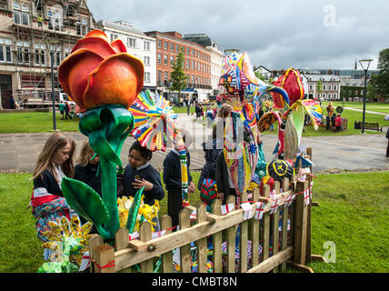 Exeter, UK. Freitag, 13. Juli 2012. Kinder schauen Sie sich die riesigen Fiberglas Harz Blumen geschmückt durch die Kinder Schule als Teil der Farben der Commonwealth-Jubiläum-Kunstprojekt über Exeter Kathedrale grün Stockfoto