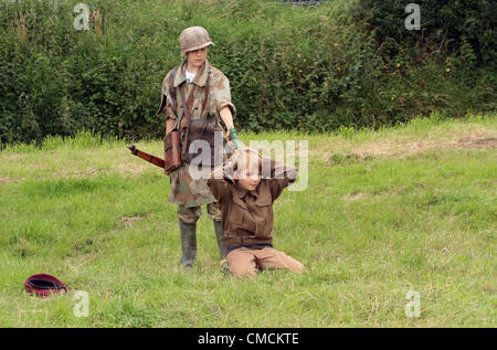 Die weltweit größte jährliche militärische Reenactment Veranstaltung begann seinen fünf-Tage-Lauf The War and Peace Show in Hop Farm, Paddock Wood, Kent im Vereinigten Königreich 18.July.2012 Enthusiasten aus der ganzen Welt in historischen Kostümen und Accessoires teilnehmen in fünf Tagen von mock Schlachten und Szenen aus der ersten und zweiten Weltkrieg.  Kind in deutscher uniform führt Häftling mit einem Gewehr auf der Rückseite des Kopfes Stockfoto