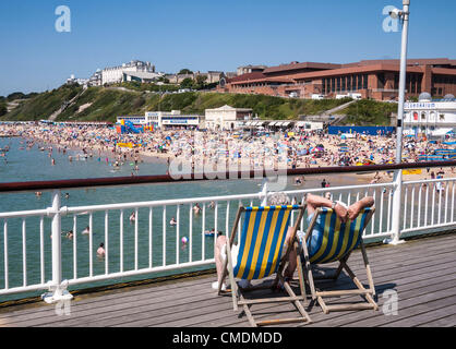 Bournemouth, Paar entspannen in Liegestühlen auf der Pier, mit Blick auf den überfüllten Strand in heißem Sommerwetter, Dorset, England, Großbritannien Stockfoto