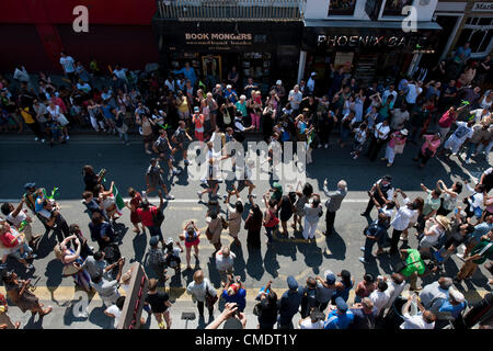 Der Olympische Fackellauf kommt Coldharbour Lane in Brixton, London, UK. Die Fackelträger durch die Polizei in der grauen Sportswear geschützt ist und das Relais ist von Sponsoren Fahrzeuge voraus. 26. Juli 2012. Stockfoto