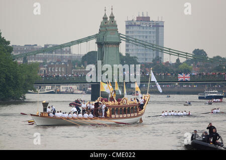 London, UK. Freitag, 27. Juli 2012. Das Olympische Feuer ist während des letzten Tages des Olympischen Fackellaufs von Ruderern an Bord der Royal Barge Gloriana hinunter den Fluß Themse von Hampton Court, den Tower of London gerudert. Hier geht die Barge Hammersmith Bridge. Stockfoto