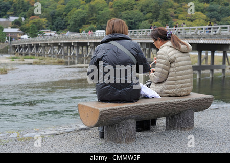 zwei japanische Frauen Essen Sushi vor der Togetsu-Kyo Brücke in Arashiyama, Kyoto, Japan Stockfoto