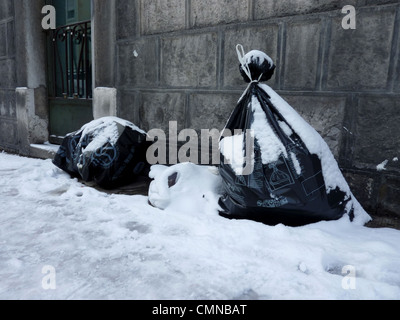 Müllsäcke, bedeckt mit Schnee und neben einer Wand auf der Straße Stockfoto