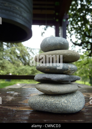 Zen Steinen auf ein Stück Holz neben einer Fischrechte Glocke in einem park Stockfoto