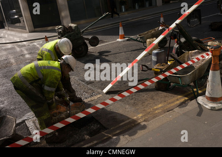 Bautrupp Schleifen auf der Fahrbahn, umgeben von Diagonalen von roten und weißen Streifen ihrer Website arbeiten. Stockfoto