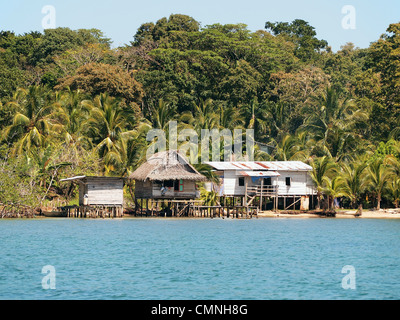 Rustikale Häuser auf Stelzen über dem Meer mit üppiger tropischer Vegetation im Hintergrund, Bocas del Toro, Panama, Mittelamerika Stockfoto