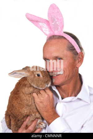 Lächelnder Mann trägt Hasenohren und hält ein Kaninchen. Stockfoto