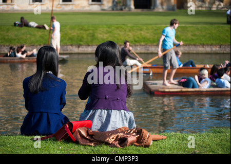 Rückansicht der beiden Mädchen sitzen am Ufer des Flusses Cam Cambridge mit Menschen Stechkahn fahren im Hintergrund. Stockfoto