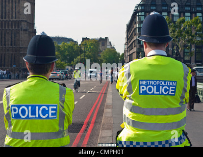 Londoner Metropolitan Police Officers Rückansicht mit Tabards im Dienst an der Westminster Bridge rote Route Verkehrslinien Houses of Parliament London UK Stockfoto
