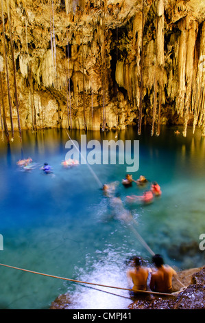 VALLADOLID, Mexiko – einheimische und besuchende Schwimmer genießen das kristallklare Wasser von Cenote X'kakah in der Nähe von Valladolid, Yucatan. Das natürliche Kalkstein-Schwimmloch verfügt über dramatische Stalaktiten, die von der Decke hängen und durch eine kleine Öffnung darüber natürliches Licht erhalten. Dieser unterirdische Pool ist Teil des riesigen Netzes unterirdischer Wasserstraßen unter der Halbinsel Yucatan. Stockfoto