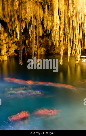 VALLADOLID, Mexiko – einheimische und besuchende Schwimmer genießen das kristallklare Wasser von Cenote X'kakah in der Nähe von Valladolid, Yucatan. Das natürliche Kalkstein-Schwimmloch verfügt über dramatische Stalaktiten, die von der Decke hängen und durch eine kleine Öffnung darüber natürliches Licht erhalten. Dieser unterirdische Pool ist Teil des riesigen Netzes unterirdischer Wasserstraßen unter der Halbinsel Yucatan. Stockfoto