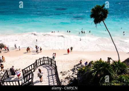 Menschen schwimmen in den kleinen Wellen des karibischen Meeres von einem der schönen weißen, sandigen Strände neben den Maya Zivilisationen Ruinen von Tulum auf der östlichen Küste der mexikanischen Halbinsel Yucatan. Im Vordergrund steht die Partei der Treppe von der archäologischen Stätte hinunter zum Strand unten. Stockfoto