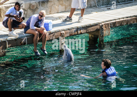 PLAYA DEL CARMEN, Mexiko – Besucher interagieren mit einem Großen Delfin im kristallklaren Wasser des Xcaret Parks. Die schlanken Meeressäuger gleiten in der Nähe der Teilnehmer und bieten eine Begegnung aus nächster Nähe in diesem beliebten Öko-archäologischen Park an Mexikos Riviera Maya. Stockfoto