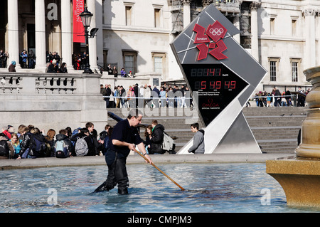 Ein Mann Poolreinigung Brunnen am Trafalgar Square in London mit dem Olympia 2012 Logo hinter Stockfoto