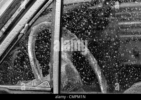 Oldtimer-Innenraum durch Regen überdachte Fenster Lenkrad in Plastik verpackt. Schwarz und weiß. Stockfoto