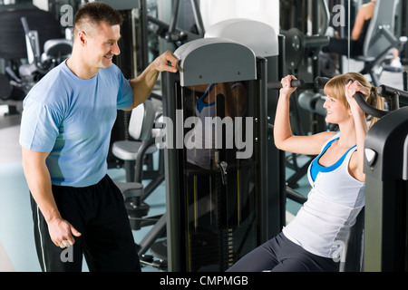 Junge Frau Übung auf Schulter-Presse-Maschine mit personal trainer Stockfoto