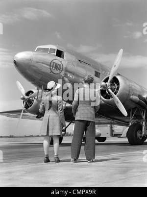 1940ER JAHRE RÜCKANSICHT DES JUNGEN & MÄDCHEN STEHEN ZUSAMMEN BETRACHTEN PROPELLERFLUGZEUG IM FREIEN Stockfoto