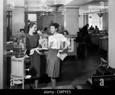 1940ER JAHREN ZWEI FRAUEN BÜROANGESTELLTEN DURCH BÜRO STEHEN WASSER KÜHLER SPRECHEN Stockfoto