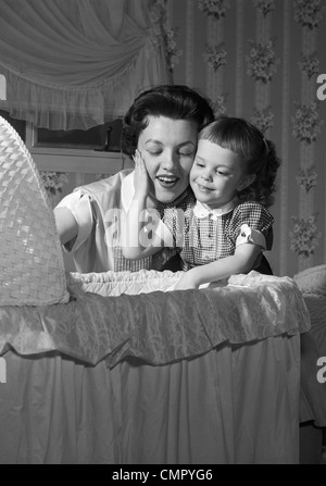 1950ER JAHRE BABY MUTTER & TOCHTER BEWUNDERN IN WIEGE Stockfoto