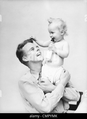 1930ER JAHREN VATER HOLDING BABY IN ARME LÄCHELND MILCHFLASCHE Stockfoto