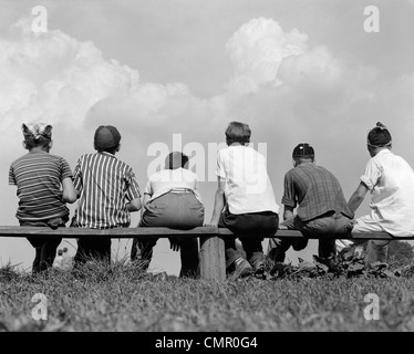 RÜCKANSICHT DER 1960ER JAHRE VON SECHS JUNGE BASEBALL-SPIELER AUF DER BANK SITZEN Stockfoto