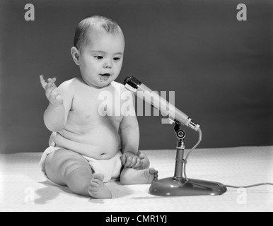 1960ER JAHRE BABY IN WINDELN INS MIKROFON SPRECHEN Stockfoto