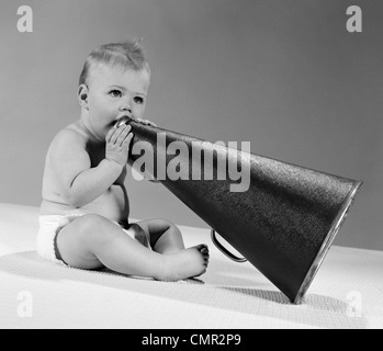 1960ER JAHRE BABY IN WINDELN SITZEN HOLDING MEGAPHON Stockfoto