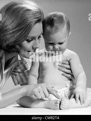 1960ER JAHREN NAHAUFNAHME VON MUTTER ZÄHLEN ZEHEN DES SITZENDEN BABY SPIELT DIESES KLEINE SCHWEINCHEN Stockfoto