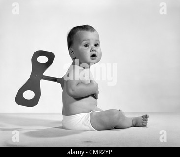 BABY-1960S 1970S SITZT IN WINDEL MIT WINDUP SCHLÜSSEL IN SEINEM RÜCKEN Stockfoto