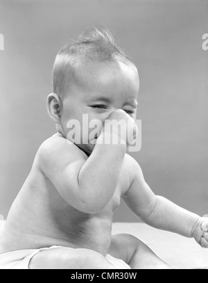 1950ER JAHRE BABY MIT GESCHLOSSENEN AUGEN, DIE NASE ZU HALTEN Stockfoto