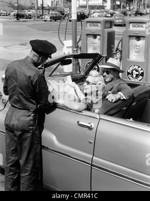 1950ER JAHREN PAAR MIT KARTE IM AUTO CABRIO FRAGEN ANFAHRT VOM TANKWART Stockfoto
