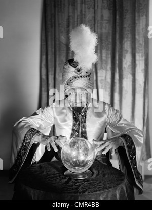 1950ER JAHRE PORTRAIT MANN WAHRSAGER SWAMI WAHRSAGERIN TRAGEN ROBE UND FEDER IN TURBAN BLICK AUF CRYSTAL BALL Stockfoto