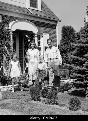 1940S 1950S FAMILIE VON VIER ZU FUß AUS HAUS MIT PICKNICK-KÖRBE THERMOS & KRUG Stockfoto