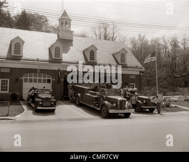 1950S 1960S FREIWILLIGER FEUERWEHRMANN UND FEUERWEHRAUTOS GEPARKT VOR FEUERWEHRHAUS Stockfoto