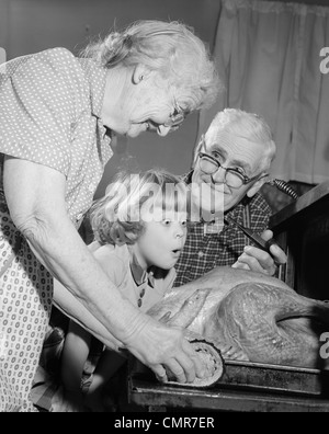 1950S 1960S BEGEISTERT KLEINE MÄDCHEN ENKELIN MIT GROßELTERN BEOBACHTETE TRUTHAHN AUS DEM OFEN KOMMT Stockfoto