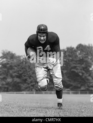 1940ER JAHREN FOOTBALL PLAYER HOLDING FUßBALL LAUFEN VORWÄRTS BLICK IN DIE KAMERA Stockfoto