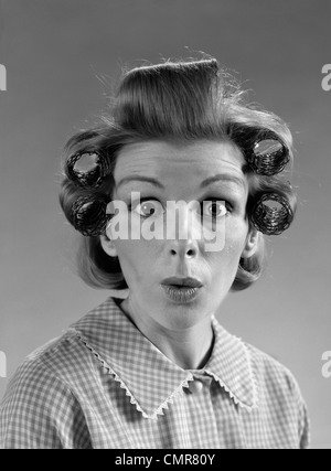 1960ER JAHRE PORTRAIT FRAU MIT HAAREN IN ROLLEN EYES WIDE MIT ÜBERRASCHUNG Stockfoto