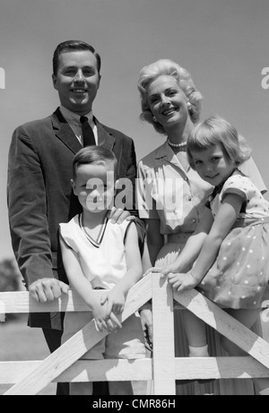 1950S 1960S PORTRAIT LÄCHELND FAMILIE VATER MUTTER SOHN TOCHTER HINTER WEIßEN ZAUN IM FREIEN Stockfoto