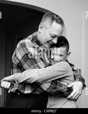 1950S 1960S LÄCHELN VATER UND SOHN UMARMT INDOOR Stockfoto