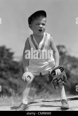 1930ER JAHRE JUNGE TRAGEN BASEBALL-MÜTZE & HANDSCHUH BENT OVER MIT HANDS ON KNIE SCHREIEN Stockfoto