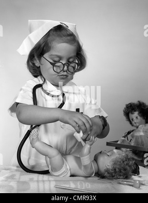 1950S 1960S MÄDCHEN TRAGEN KRANKENSCHWESTER UNIFORM BRILLE SETZEN BANDAGE AM ARM DER PUPPE Stockfoto