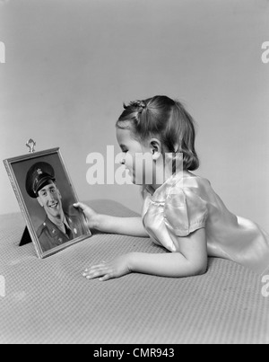 1940ER JAHRE KIND MÄDCHEN MIT BLICK AUF GERAHMTE BILD VON IHREM VATER A SOLDAT IN UNIFORM Stockfoto