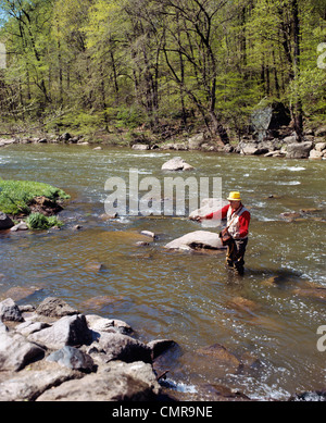 1970ER JAHRE MANN FLIEGENFISCHEN IN STREAM TRAGEN KAUTSCHUK WATSTIEFEL Stockfoto