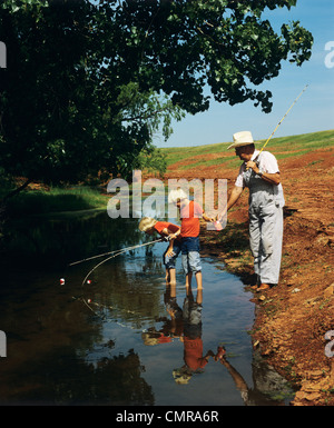 1970S 1980S TWIN JUNGEN FISCHEN IN STREAM MIT GROßVATER Stockfoto