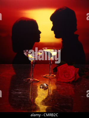 1970ER JAHRE PORTRAIT SILHOUETTE PAAR MANN FRAU BEI SONNENUNTERGANG GOLD ENGAGEMENT TRAURINGE WEINGLÄSER RED ROSE Stockfoto