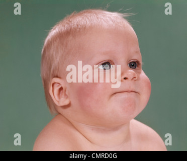 1960ER JAHRE PORTRAIT DER BLONDE BABY PAUSBACKEN MIT LUSTIGEN GESICHTSAUSDRUCK Stockfoto