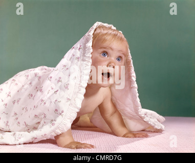 1960ER JAHRE BABY KRABBELN UND SPÄHEN AUS UNTER EINER DECKE Stockfoto