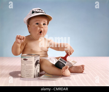 1960ER JAHRE BABY MIT LUSTIGEN GESICHTSAUSDRUCK MIT MALER MÜTZE PINSEL SITZEN DURCH DEN LACK HALTEN KÖNNEN Stockfoto